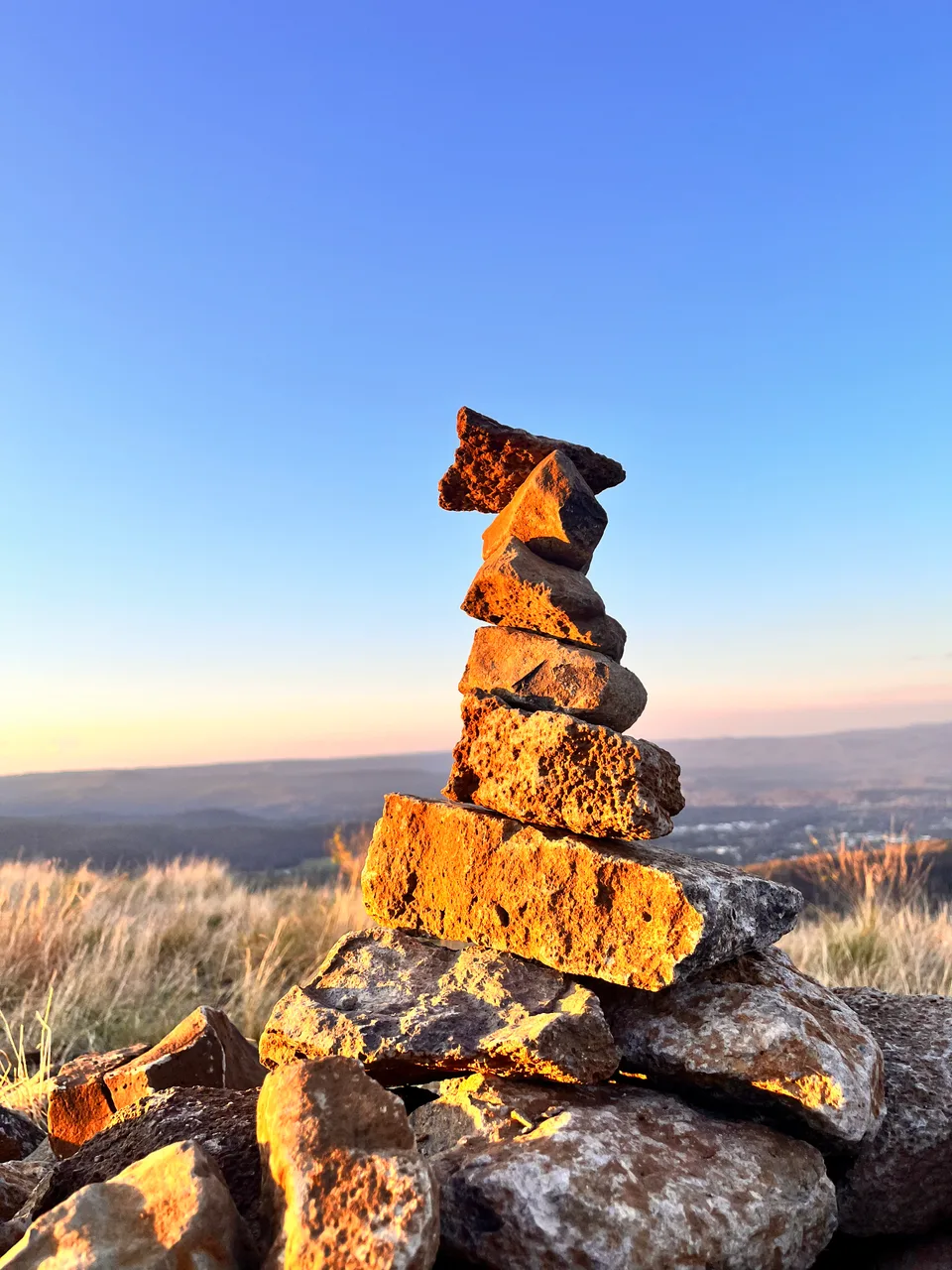 A stack of stones lit by golden sunlight beneath a clear blue sky